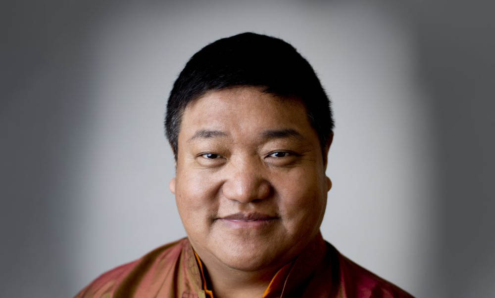 Portrait of a man smiling slightly, wearing a burnt orange shirt.
