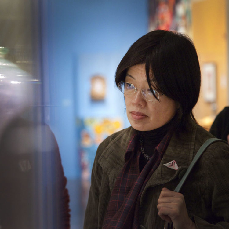 A woman wearing glasses looks intently at artwork in a glass case.