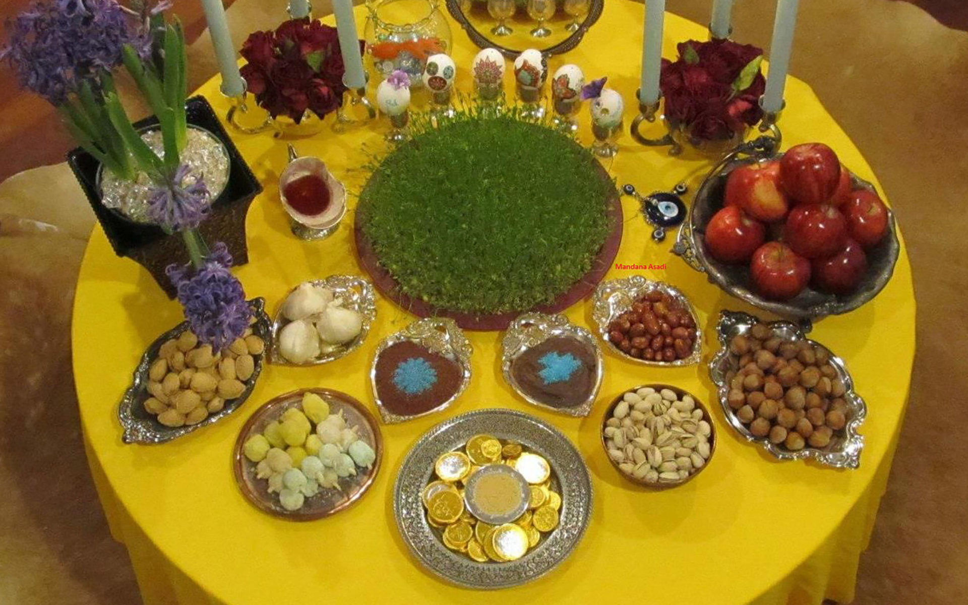 A tabled set with many dishes and candles on a yellow tablecloth.