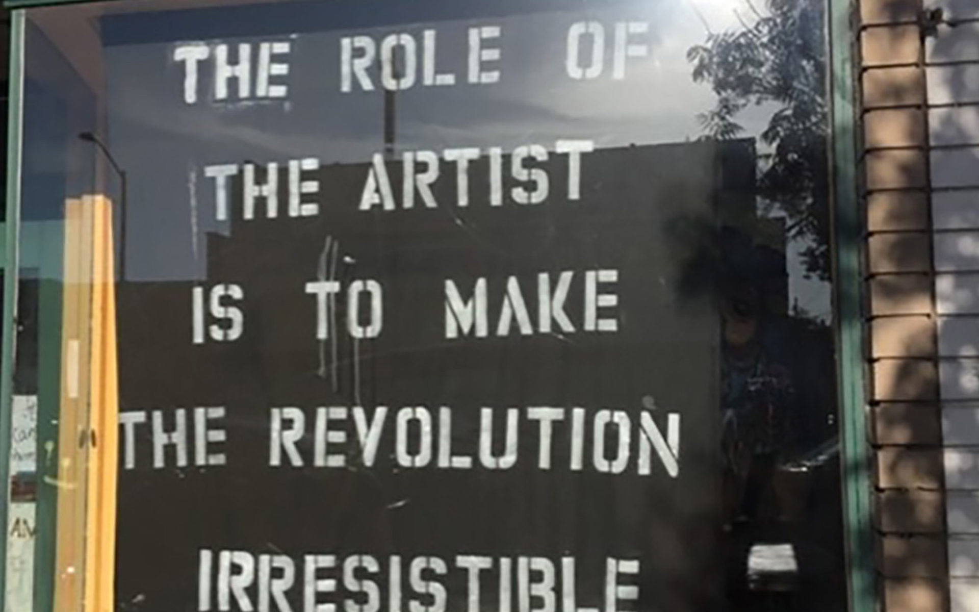 Window with a poster saying "The role of the artist is to make the revolution irresistible."