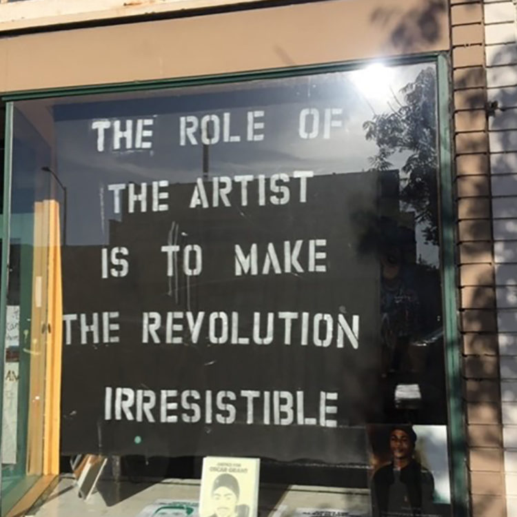 Window with a poster saying "The role of the artist is to make the revolution irresistible."