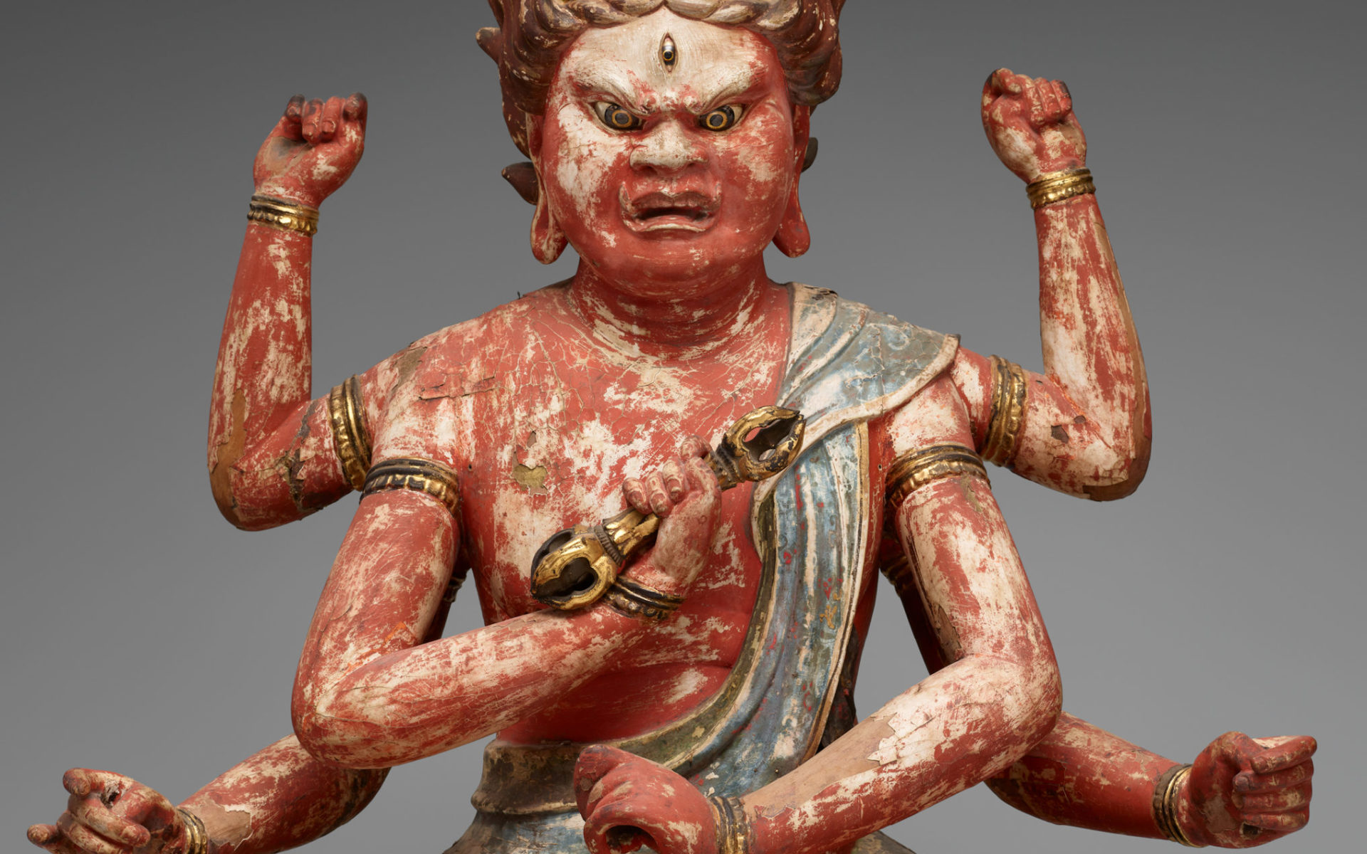 Six-armed, angry-faced, red-skinned deity.