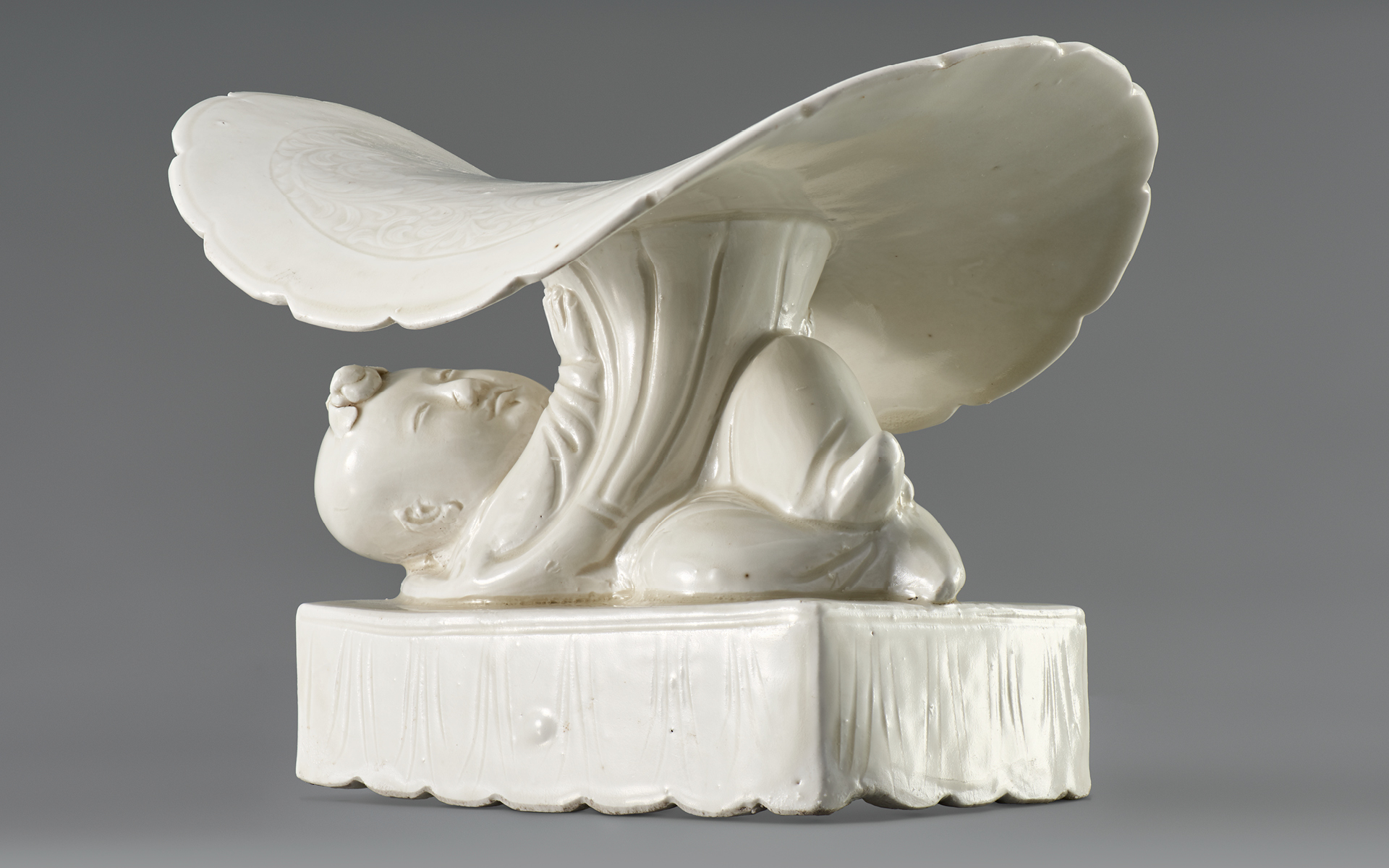 White porcelain in shape of little boy lying under a lotus leaf.