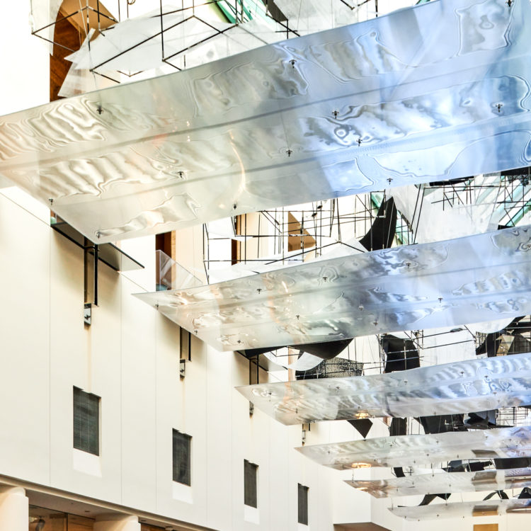 Large open space hung with large rectangular sheets of semi-transparent material from geometric rigging.