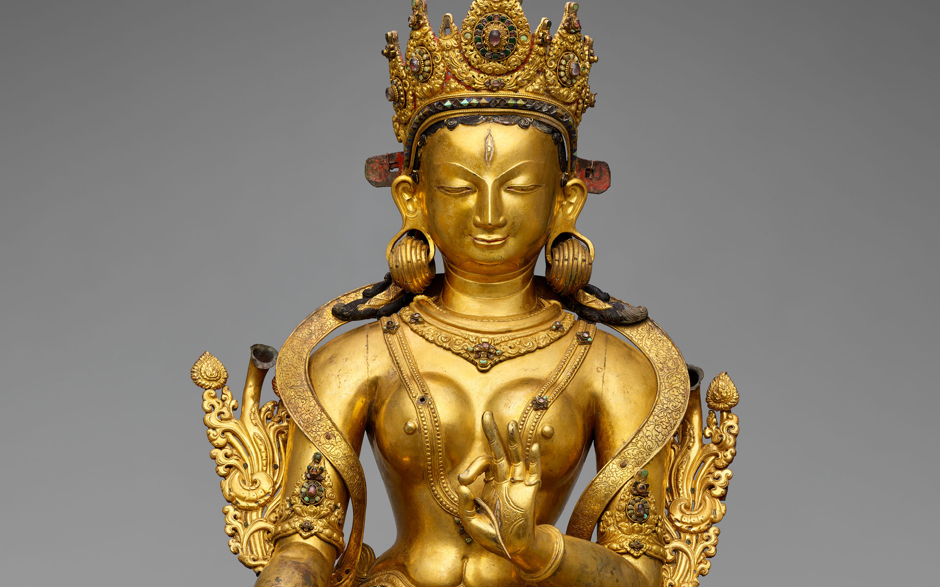 Gilded, crowned and bejeweled female figure, seated in lotus position.