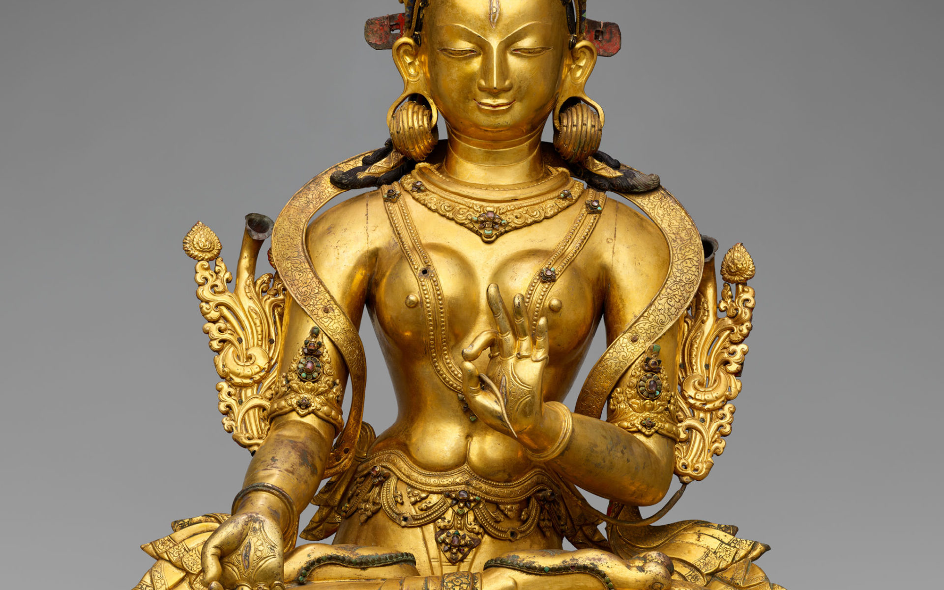 Gilded, crowned and bejeweled female figure, seated in lotus position.