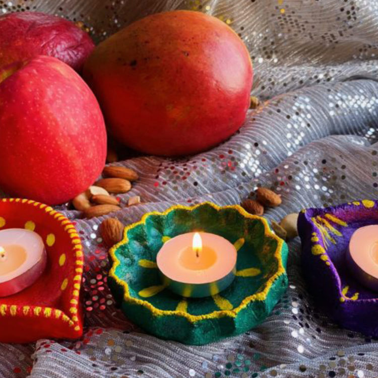 Three votive candles burn in colorfully decorated dishes, amid an apple, two mangos, and a scattering of almonds.