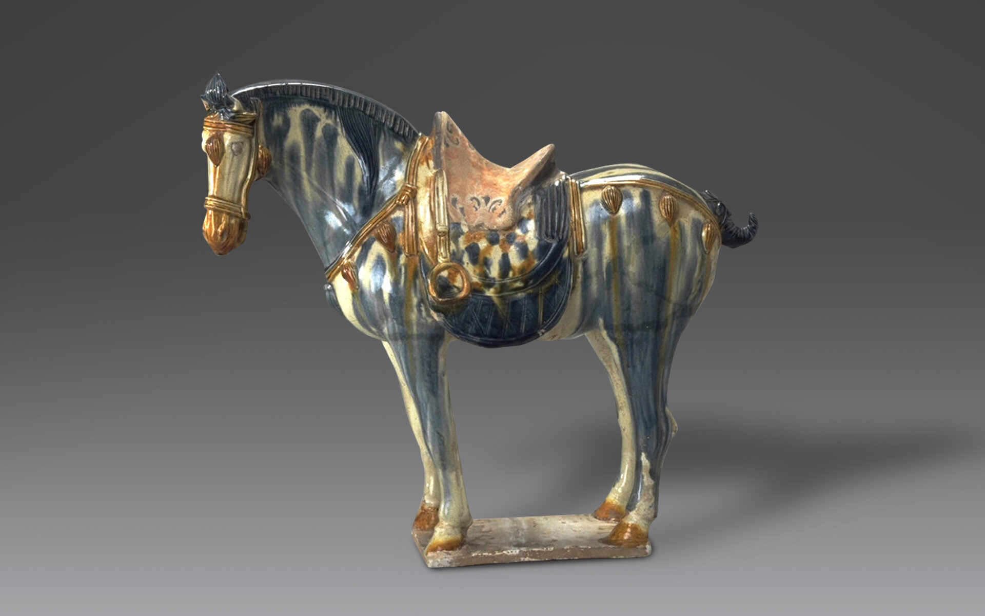 Ceramic horse with bridle and saddle glazed in blue, cream, and brown that stands over one foot tall.