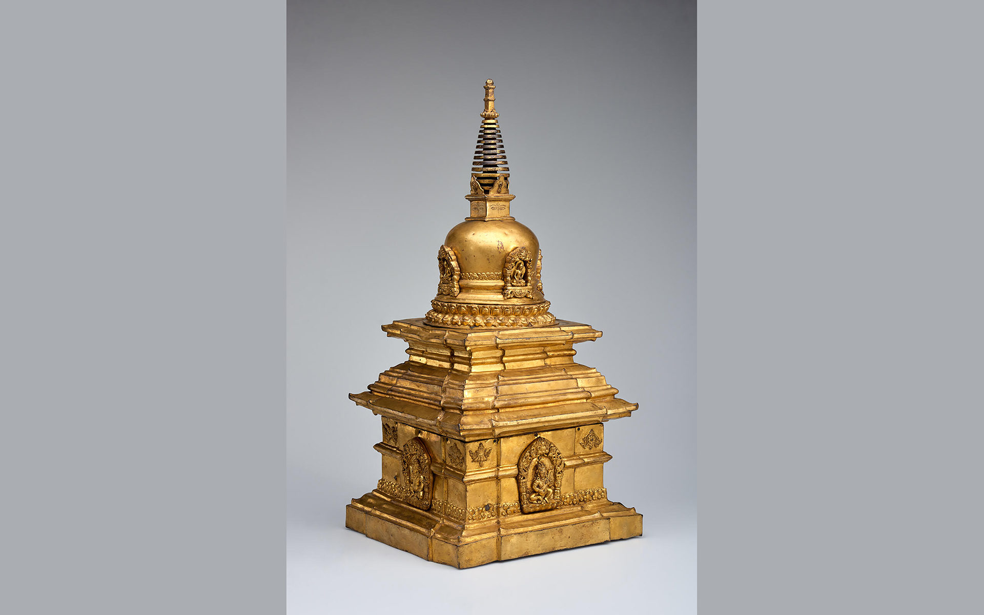 Gilded bronze sculpture of a four-sided and domed vessel with images of Buddhas on the four sides in relief.