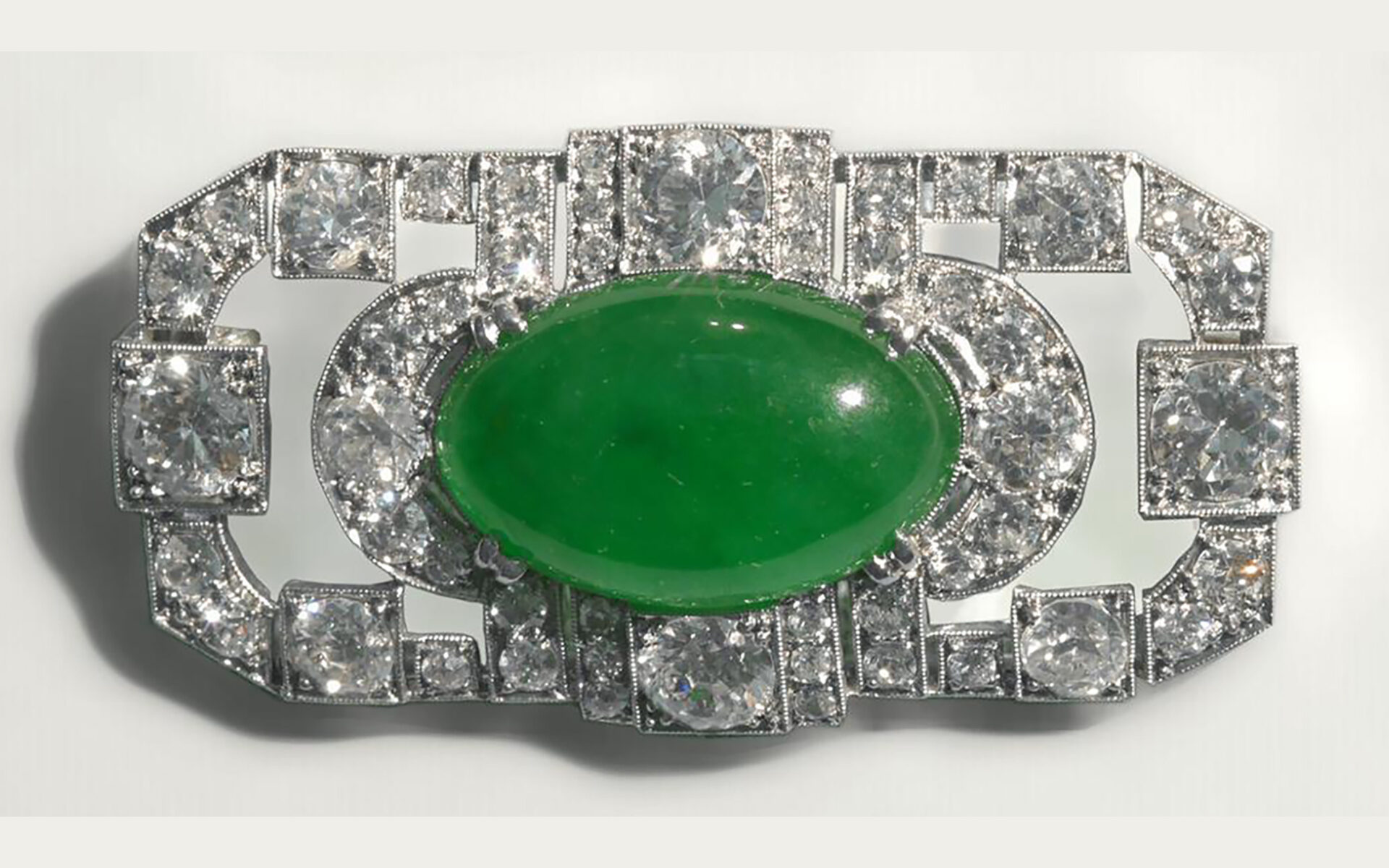 Oblong green stone set in a diamond studded silver brooch.