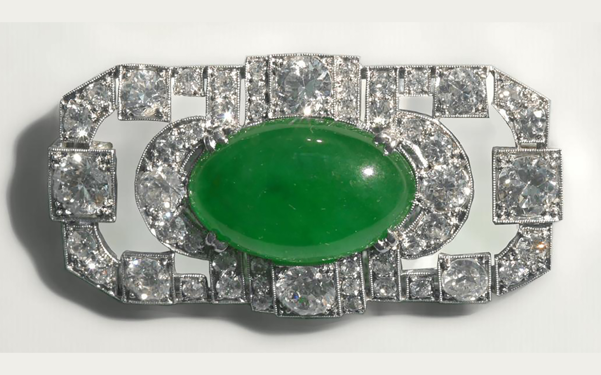 Oblong green stone set in a diamond studded silver brooch.