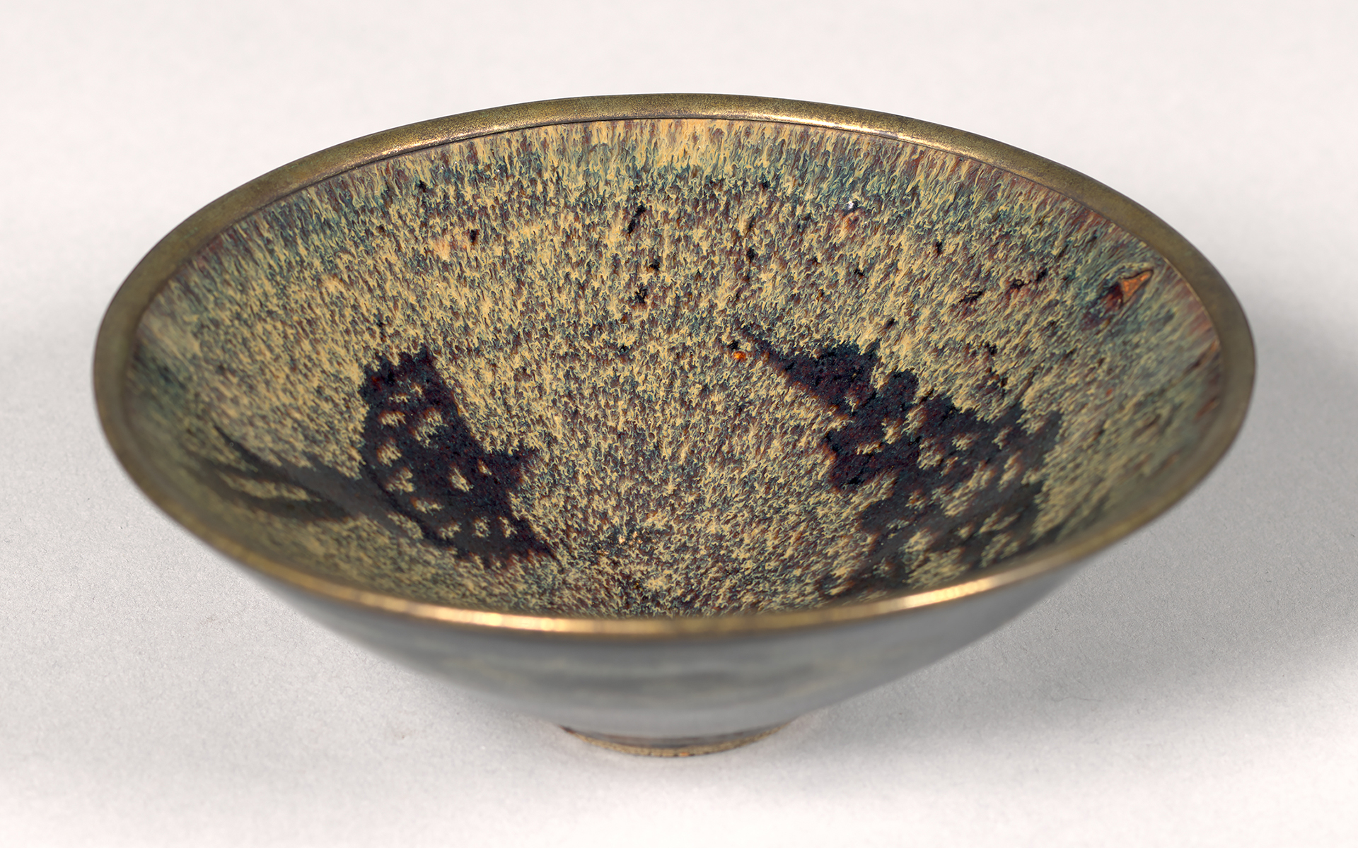 Shallow tea bowl in golden brown with darker brown spots.